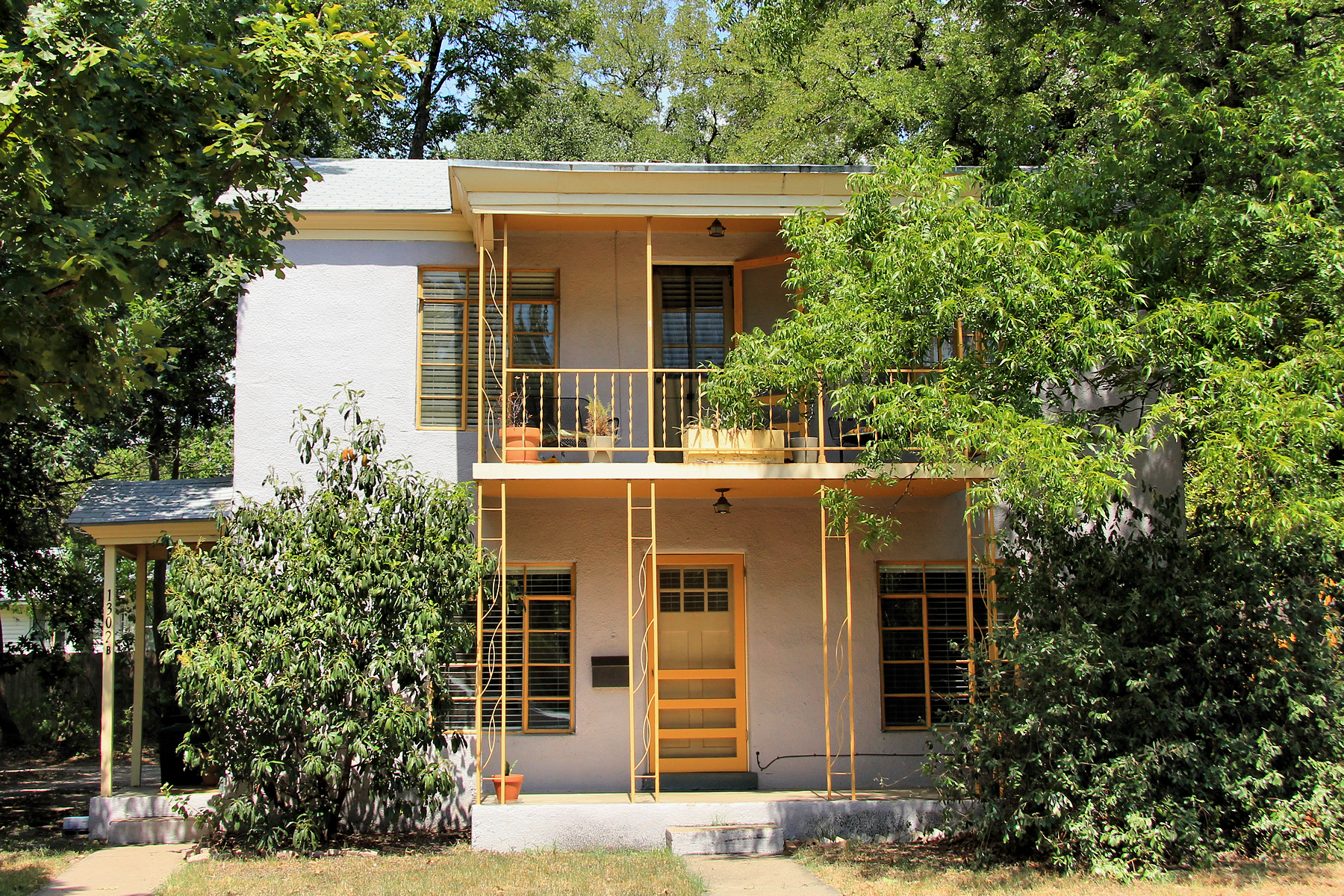 A 1948 Delwood duplex at 1302 Kirkwood Road in Cherrywood, Austin, with a two story stucco facade and trees